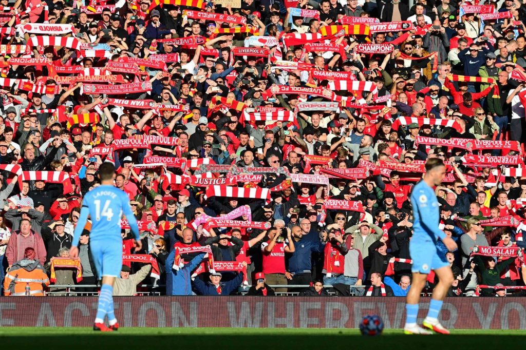 Crowd of passionate Premier League fans in red scarves cheering as players on the pitch highlight the excitement of Premier League betting.